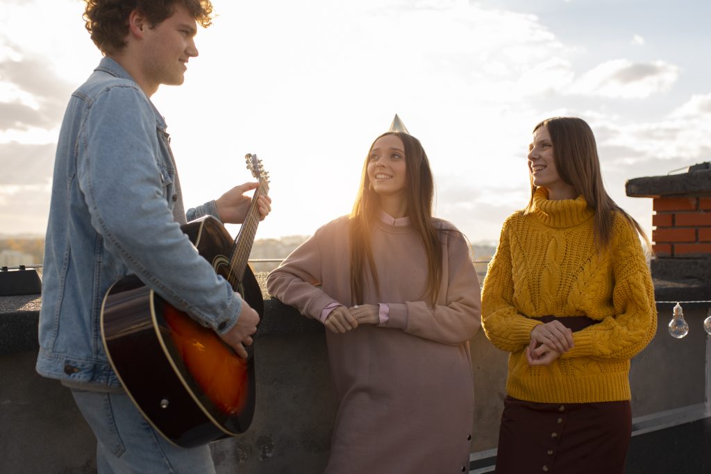 Un chico tocando la guitarra tranquilamente mientras mira a dos mujeres.